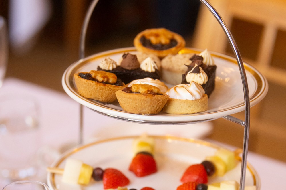 detail from an afternoon tea table setting showing finger food of bitesize cakes and fruit skewers