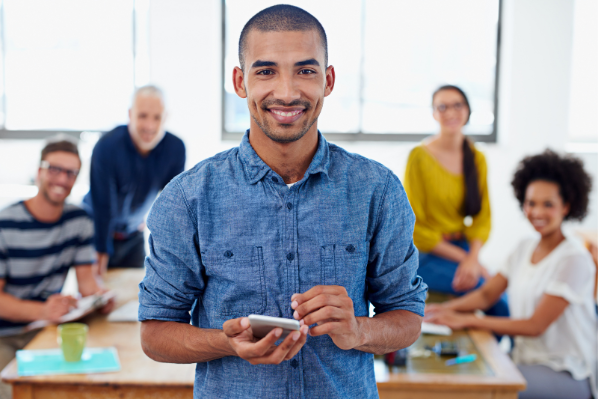 young man standing ion a room smiling with colleagues in background