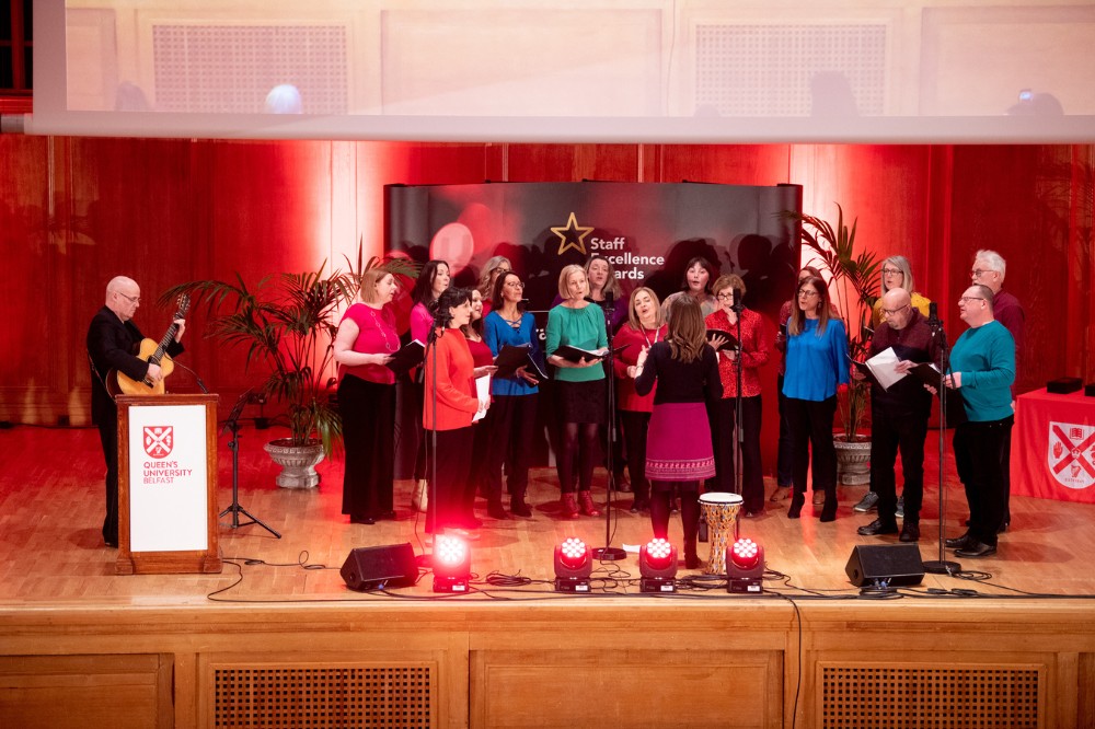 Staff Wellbeing Choir performing on stage in the Whitla Hall for the Staff Excellence Awards 2022