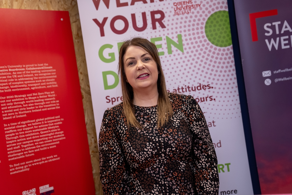 A staff member of Spectrum.Life stands smiling in front of Queen’s University Belfast Staff Wellbeing and Employee Assistance Programme display banners.