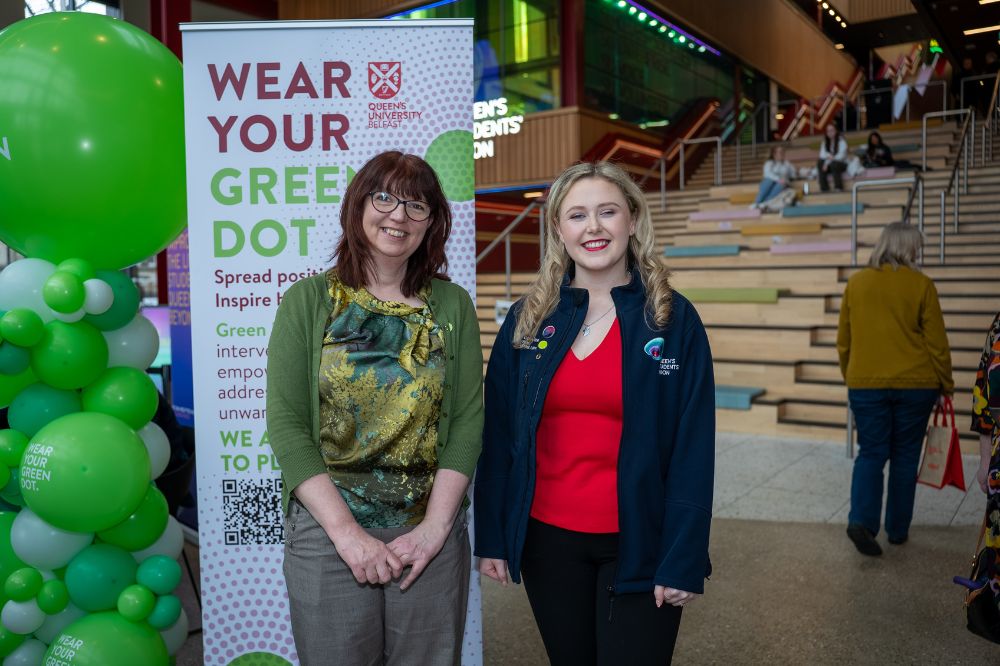 Two staff members standing beside a 'Wear Your Green Dot' banner in the Queen’s Students’ Union building.