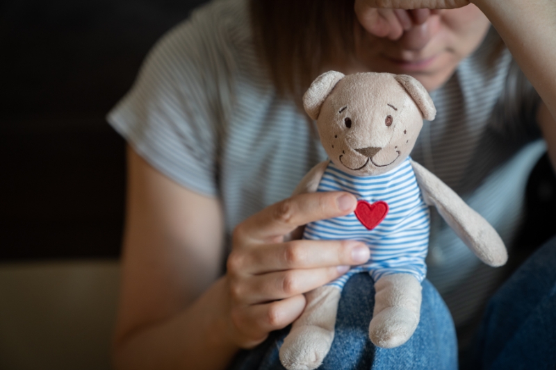 grieving young woman seated and holding a teddy bear with a red heart