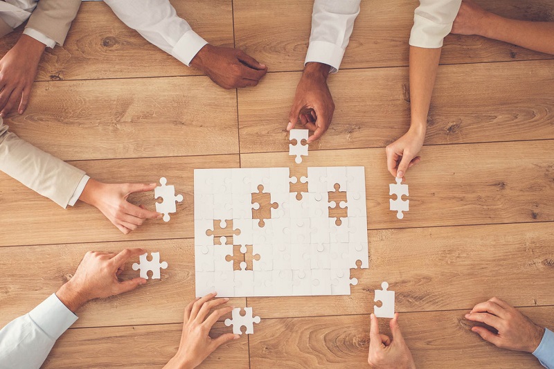 aerial view of professional people's hands piecing together a blank jigsaw on a wooden table