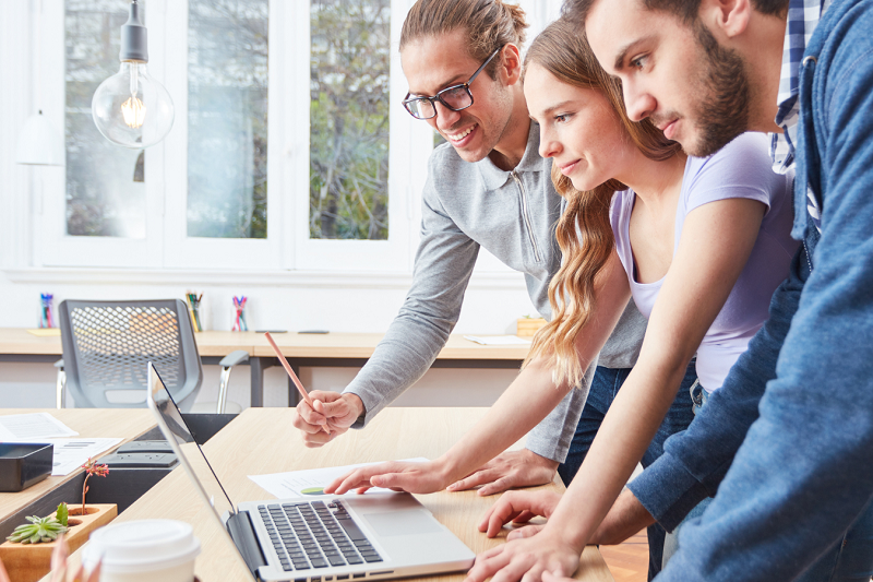 three young professionals, one female and two males, looking at a laptop in a bright, open-plan space