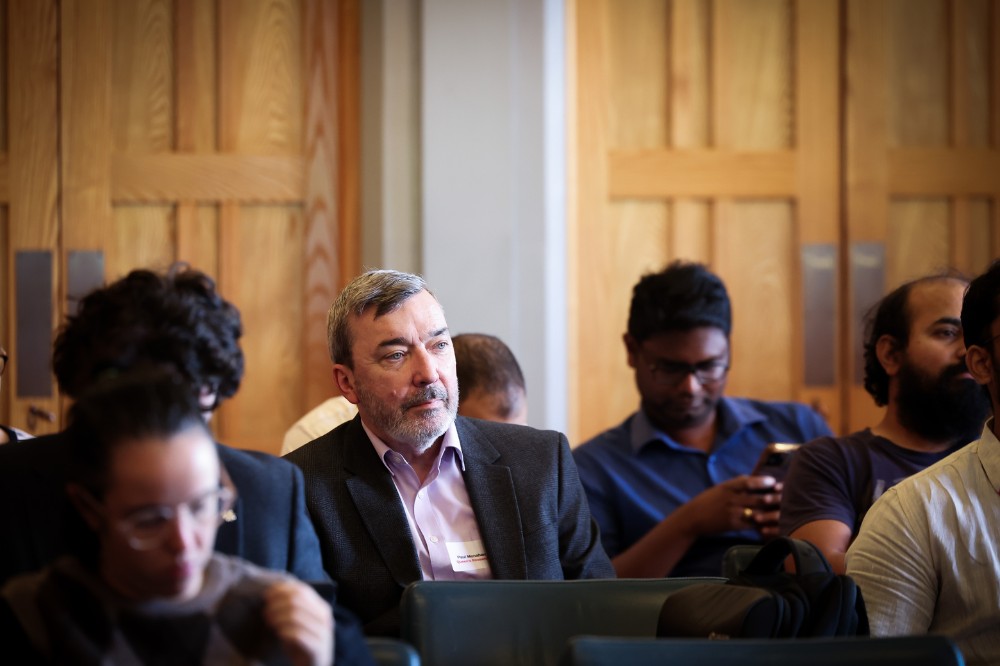 mature seated gentleman listening to a presentation alongside other attendees in a comfortable-looking, wood-paneled, indoor event space