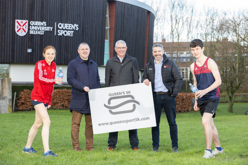 sporting students and staff standing outside the Physical Education Centre holding a Queens 5K plaque