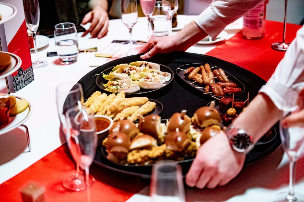 catering personnel placing a large tray of finger foods on a table at an indoor event