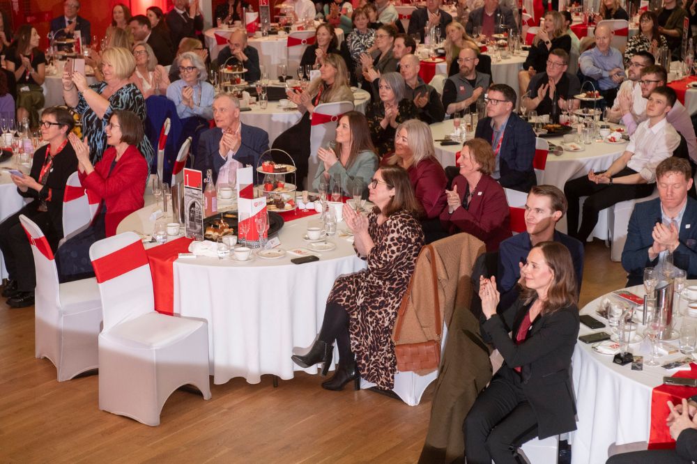 groups of people sitting at tables at an indoor event watching something off-camera and applauding