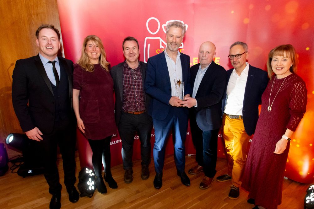 group of five men and two women posing for the camera and being presented with or collecting an award at an event