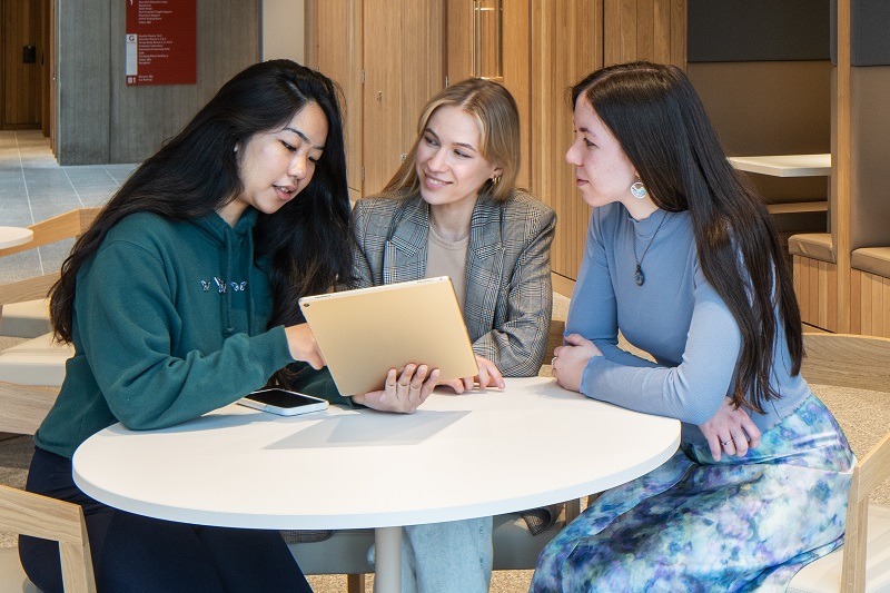 three female students chatting at a table in Queen's Business School